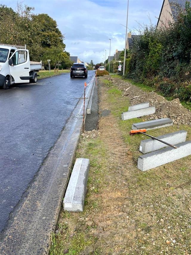 Bordures béton en cours de pose sur un lit de béton le long d'une rue