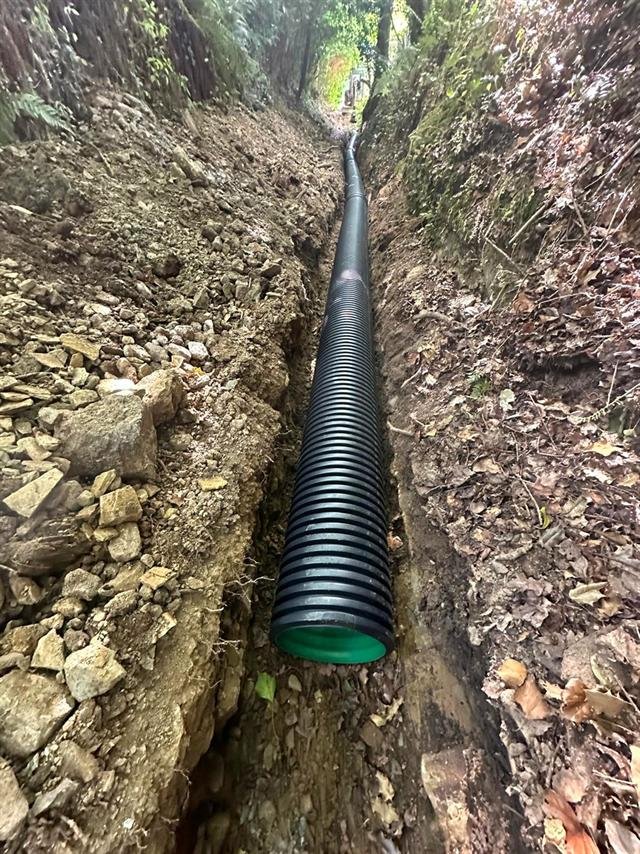 Canalisation annelée noire posée au fond d'une tranchée en sous-bois