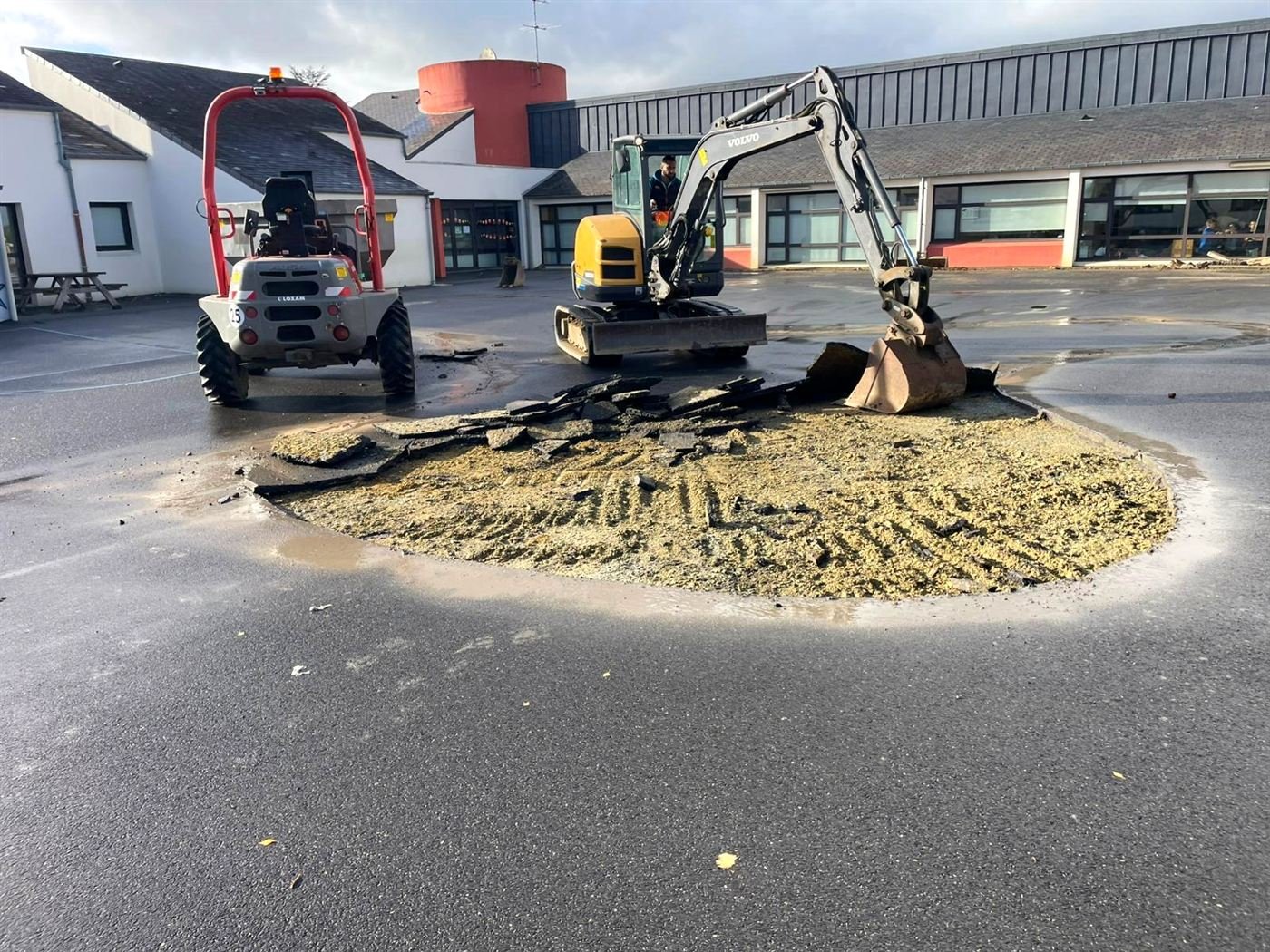 Mini-pelle et dumper retirant l'enrobé d'une cour d'école pour créer un massif rond