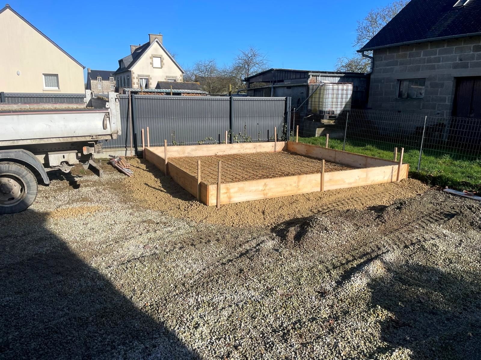 Coffrage en planches et treillis soudé posés sur un lit de gravier, prêts pour couler une dalle béton