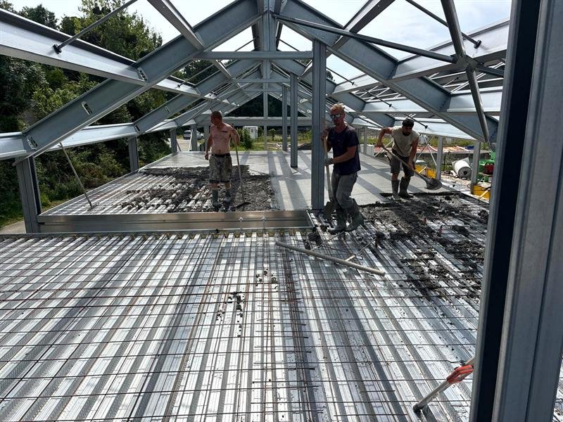 Trois maçons tirent le béton d'un plancher sur bac acier, sous une charpente métallique