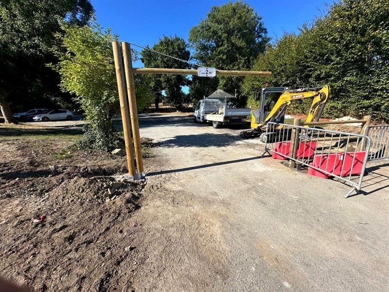 Portique en bois avec panneau hauteur maximale 2 mètres à l'entrée d'un parking, mini-pelle à côté